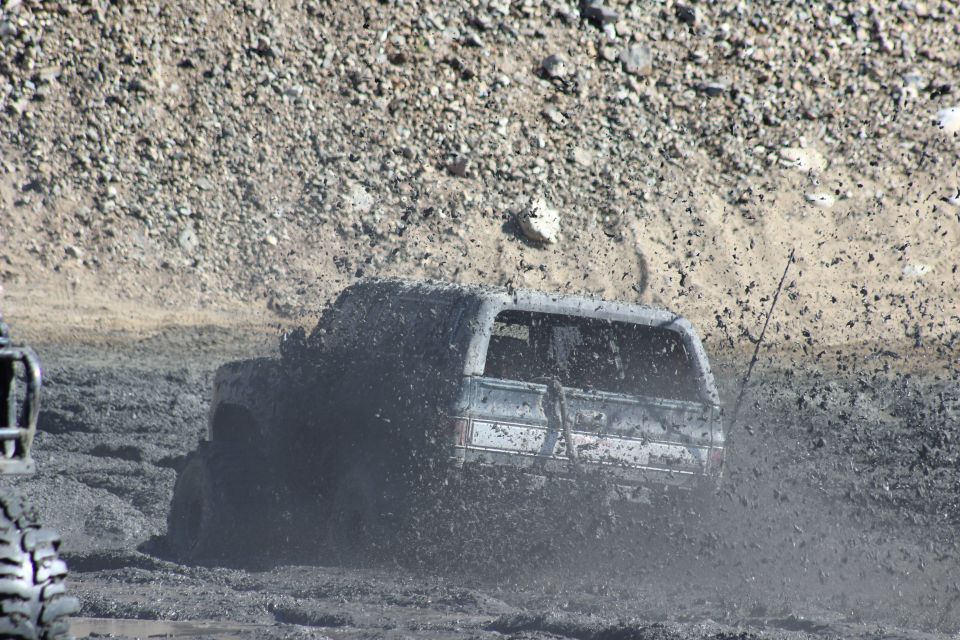 1978 Ford Bronco driving through deep mud, kicking up spray