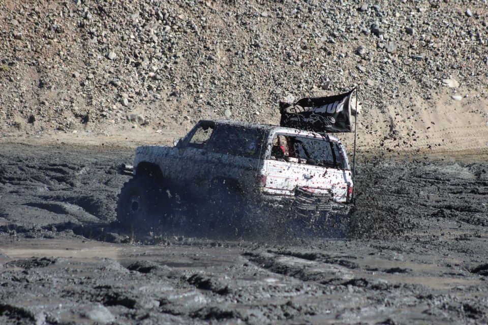 White SUV driving through thick mud, kicking up spray. Black flag attached to rear