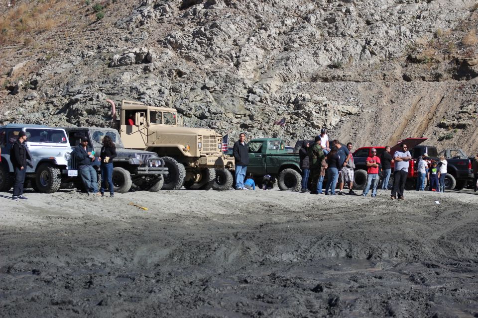 Line of off-road vehicles including Jeeps, a military truck, and a green pickup truck, with people standing around them