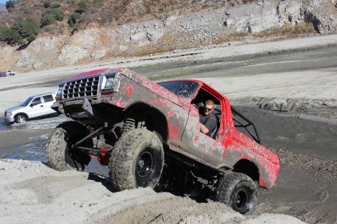 1978 Ford Bronco - This heavily modified SUV is navigating a muddy, sandy terrain with a second vehicle in the background.