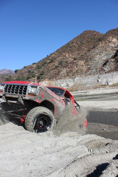 1978 Ford Bronco - A red 1978 Ford Bronco navigates a sandy terrain, its tires churning up a cloud of dust.