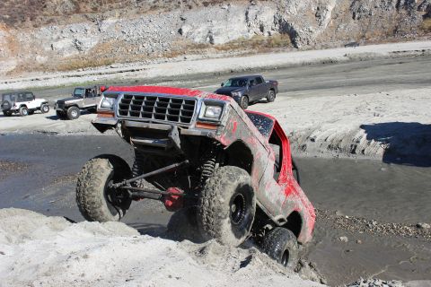1978 Ford Bronco - Multiple off-road vehicles navigate a muddy terrain with rocky hills in the background.