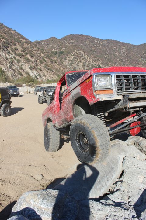 1978 Ford Bronco - Multiple off-road vehicles navigate a rocky terrain under a clear blue sky.