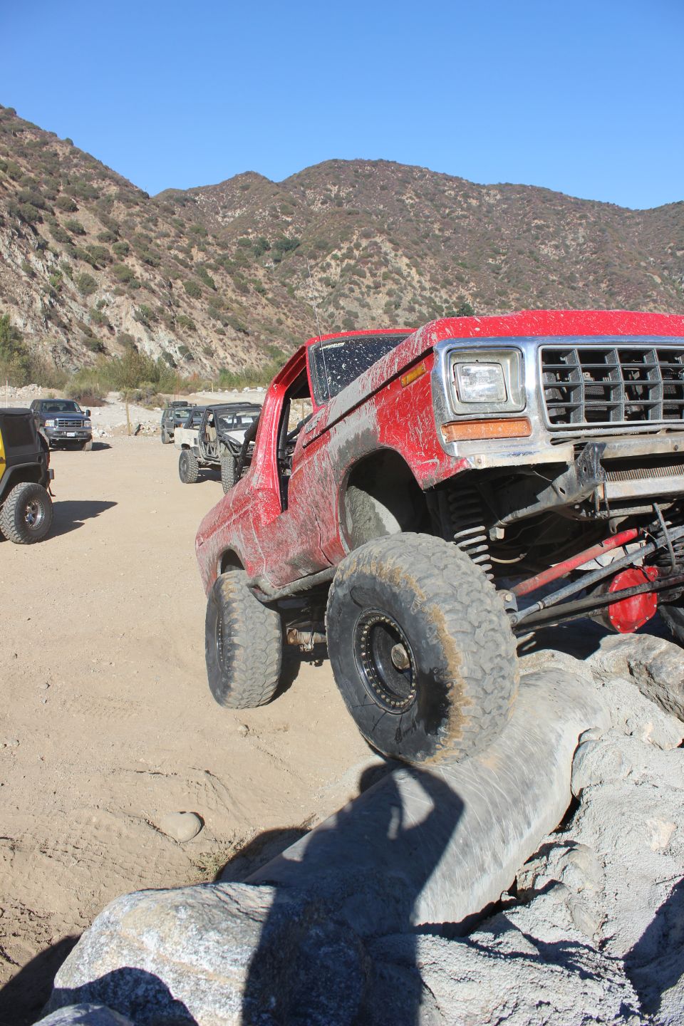 Red off-road SUV with large tires climbing over rocks, front grille visible
