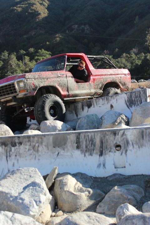 1978 Ford Bronco - A mud-covered 1978 Ford Bronco navigates a challenging off-road course with concrete barriers and large rocks.