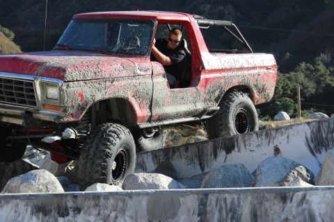 1978 Ford Bronco - This red 1978 Ford Bronco navigates a rocky obstacle course, its body caked in mud from the challenging terrain.