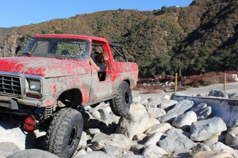 1978 Ford Bronco - A red 1978 Ford Bronco navigates a rocky terrain, covered in mud.
