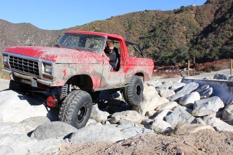 1978 Ford Bronco - A red 1978 Ford Bronco is shown navigating a rocky terrain, with its front tire lifted.