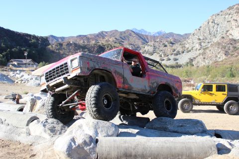1978 Ford Bronco - A red off-road SUV navigates a rocky obstacle course with a yellow Jeep in the background.
