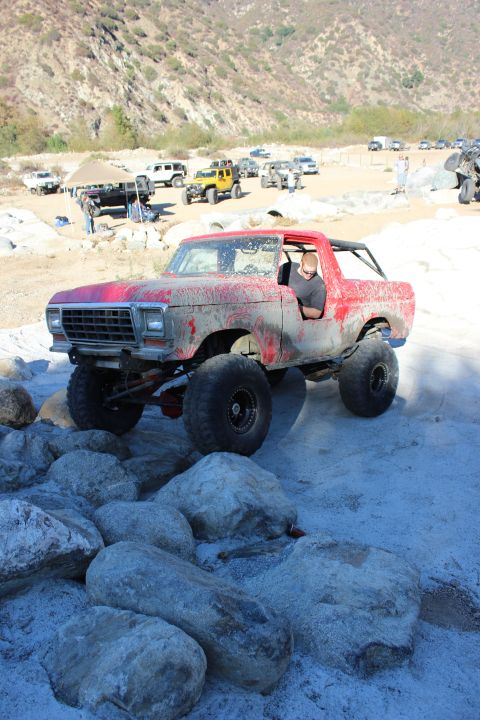1978 Ford Bronco - A red 1978 Ford Bronco is driven over rocks in a desert landscape with other vehicles present.