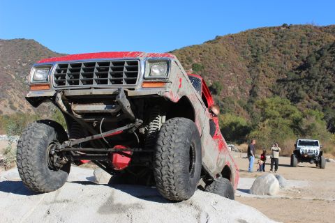 1978 Ford Bronco - A red off-road SUV navigates a rocky trail with a white SUV and people in the background.