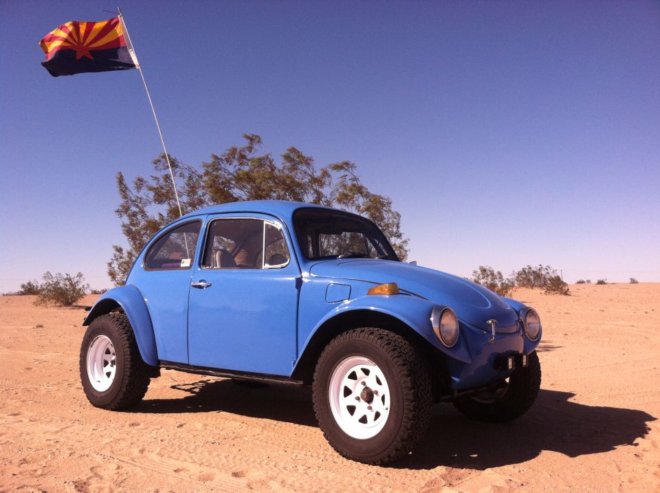 Blue Volkswagen Beetle Baja Bug with off-road tires and white rims, Arizona flag flying, parked in desert