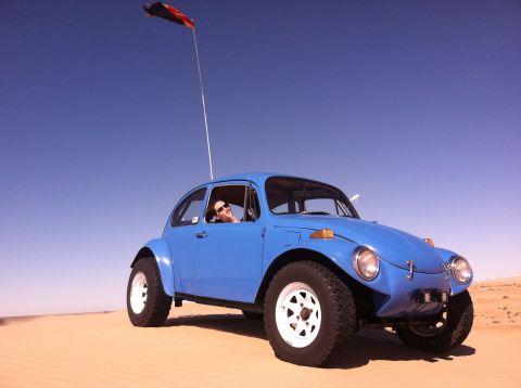 1970 Volkswagen Beetle - A blue 1970 Volkswagen Beetle dune buggy is driven across sandy terrain under a clear blue sky.