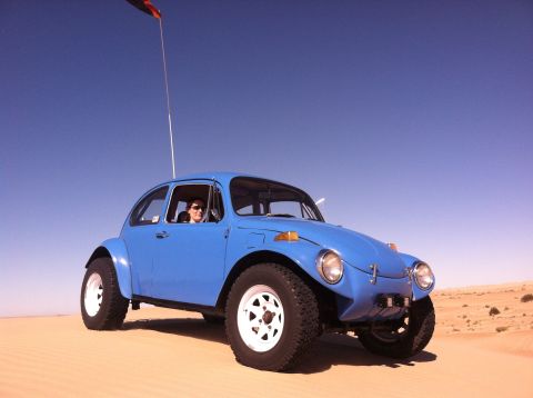 1970 Volkswagen Beetle - A blue off-road vehicle with a person driving is on a sandy terrain under a clear blue sky.