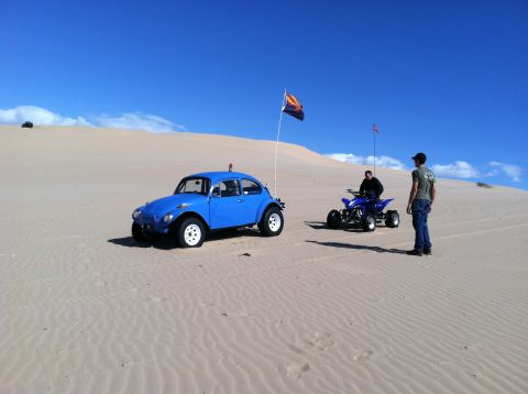 1970 Volkswagen Beetle - A blue 1970 Volkswagen Beetle and an ATV sit on sand dunes with two people nearby.