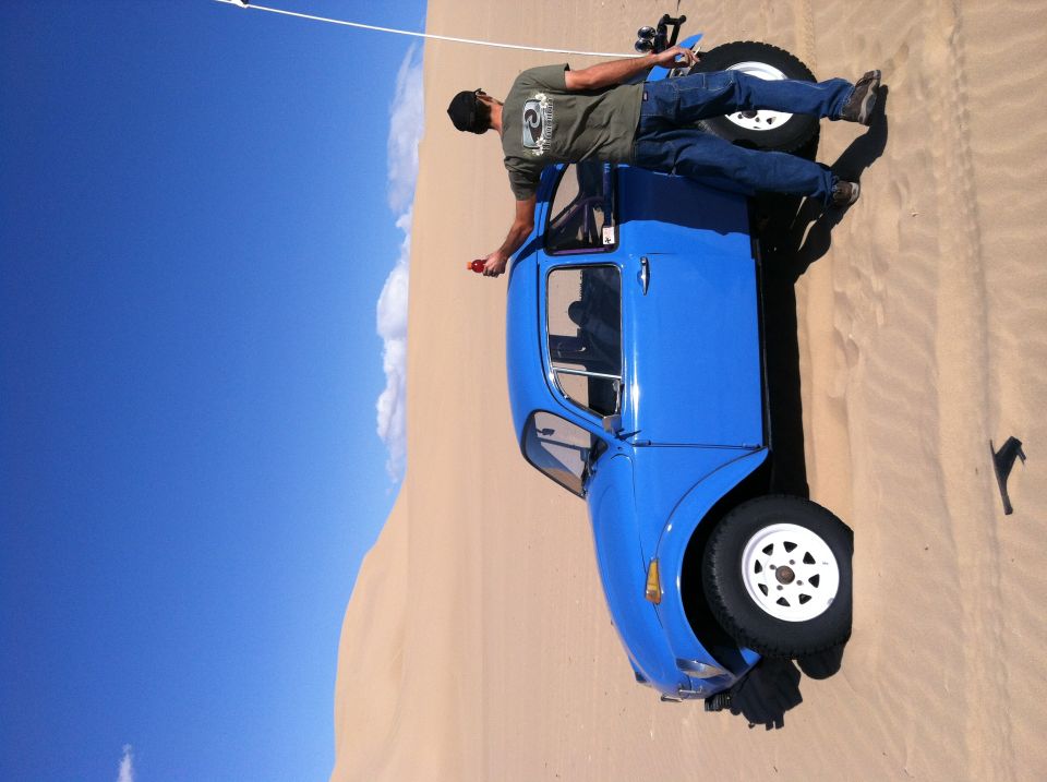 Guy lying on top of a blue dune buggy in the sand with blue sky