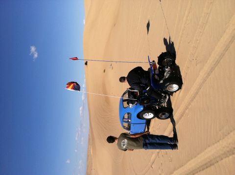 1970 Volkswagen Beetle - Two people are on a blue dune buggy on sand dunes under a clear blue sky.