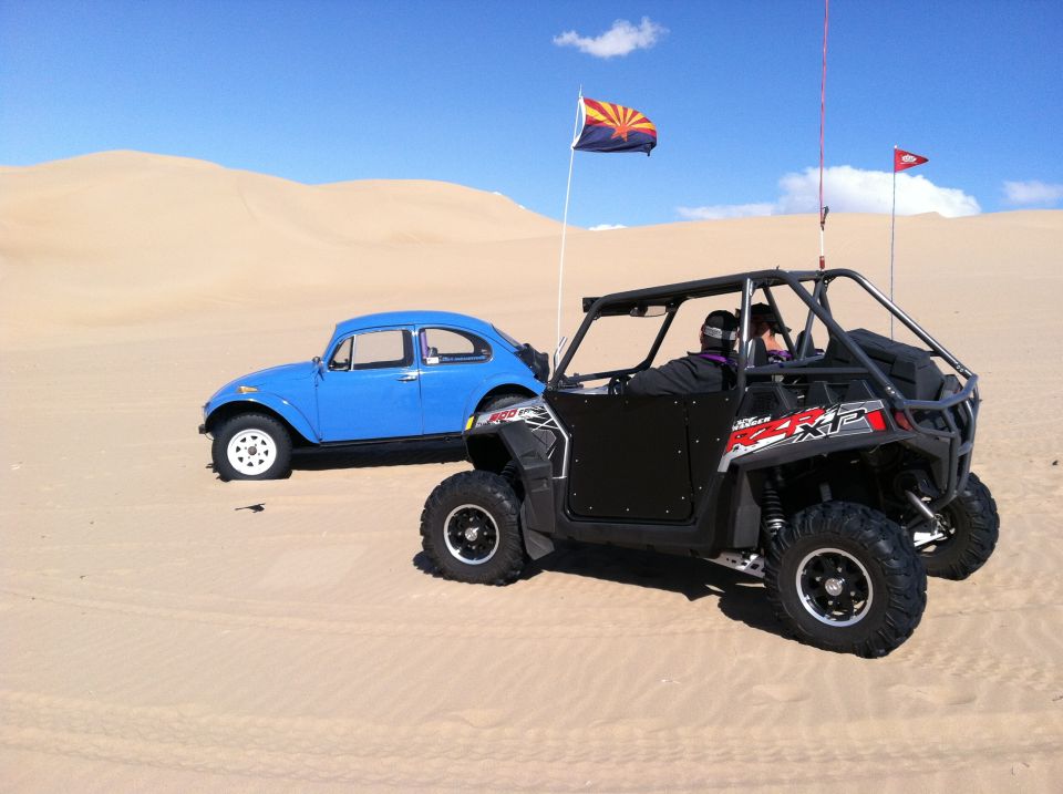 Blue 1970 Volkswagen Beetle parked in sand dunes next to a black UTV