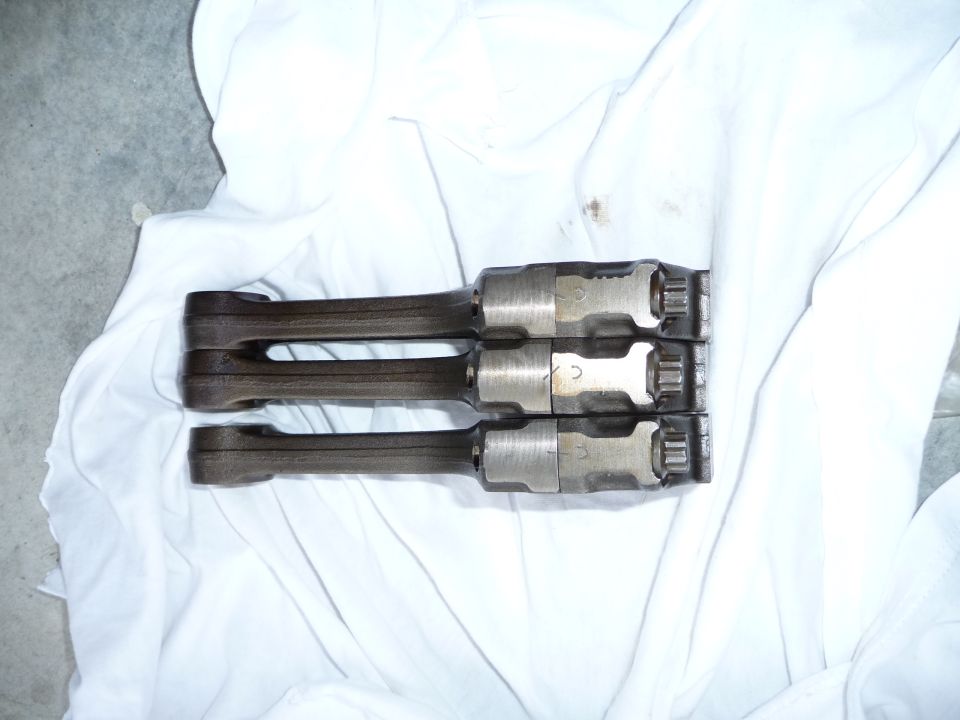 Three engine connecting rods laid on white cloth. Numbers are visible on the rods
