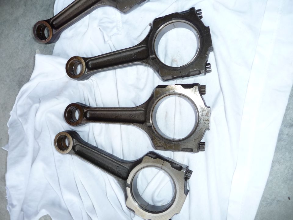 Four engine connecting rods laid out on white cloth. One rod is partially visible at the top