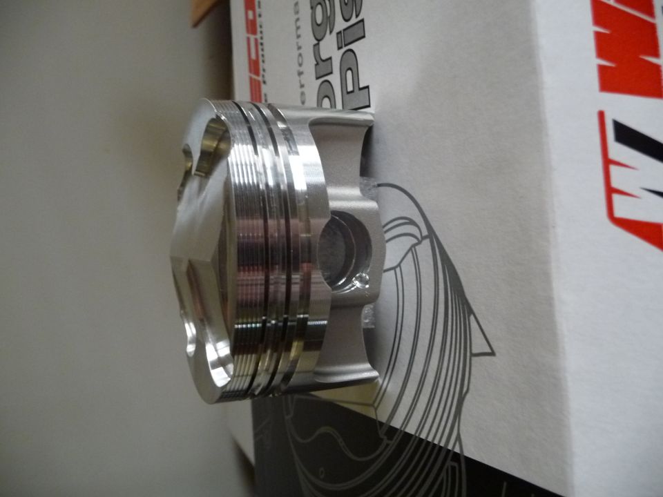 Wiseco piston with multiple compression ring grooves, resting against a box with graphics
