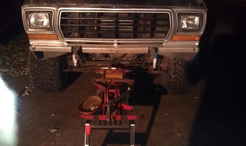 1979 Ford Bronco - The front of a truck is shown, lifted on a jack with mechanical components exposed beneath.