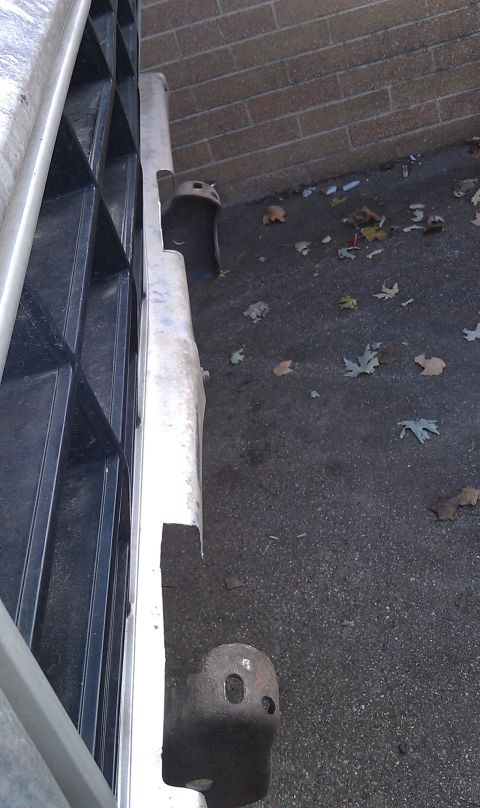 1979 Ford Bronco - A detached metal bumper section is shown next to a black grille, with fallen leaves on the asphalt.