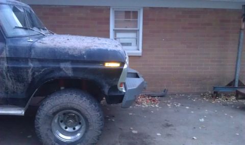 1979 Ford Bronco - A black 1979 Ford Bronco is parked in front of a brick building, showing its front corner and aftermarket bumper.