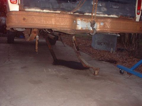 1993 Ford Bronco - Rear suspension and bumper of a truck are heavily rusted and appear to be undergoing repair.
