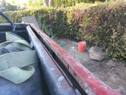 1978 Ford Bronco - Interior view of a truck bed, showing straps and a red metal bar, with a bucket and hose in the background.