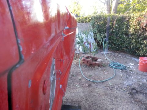 1978 Ford Bronco - The side of a red vehicle shows signs of wear and tear, with a garden hose and bucket visible in the yard.