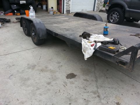 1978 Ford Bronco - A flatbed trailer is parked on a concrete surface, with tools and a bottle of water on its deck. A dark SUV is visible in the background.