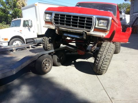 1978 Ford Bronco - A red pickup truck is loaded onto a flatbed trailer, showing its lifted suspension and front grille.