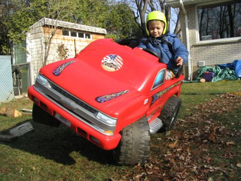 1986 Ford Bronco - A young boy wearing a helmet sits in a bright red toy truck outdoors.