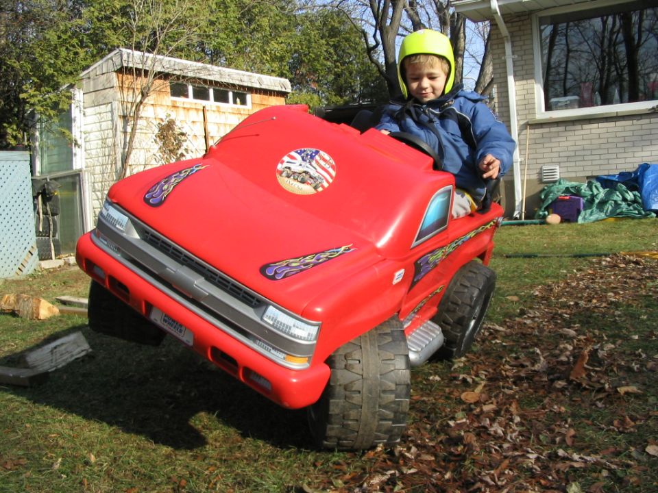 kid in a red toy truck with flame decals and an American flag sticker on the hood