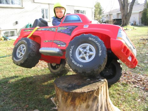 1986 Ford Bronco - A child sits in a red toy truck with flame decals, positioned precariously on a tree stump.