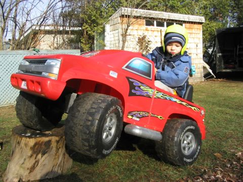 1986 Ford Bronco - A child is playing in a red toy truck with large tires, parked on a tree stump.