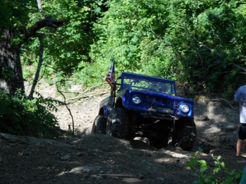 1967 Ford Mustang - A blue off-road vehicle navigates a challenging dirt trail, flying an American flag.