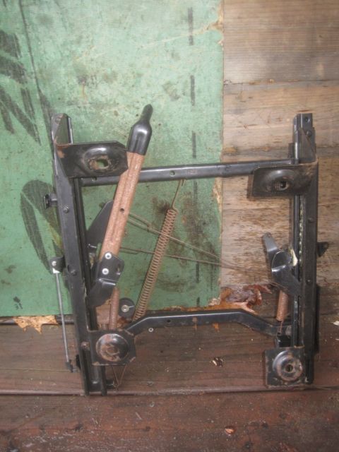 1993 Ford Bronco - Seat frame mechanism with springs and levers, likely for a vehicle, shown against a green and wood background.