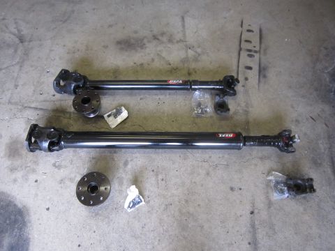2008 Jeep Wrangler - Two driveshafts, possibly for a Jeep Wrangler, are laid out with their mounting flanges and hardware on a concrete surface.