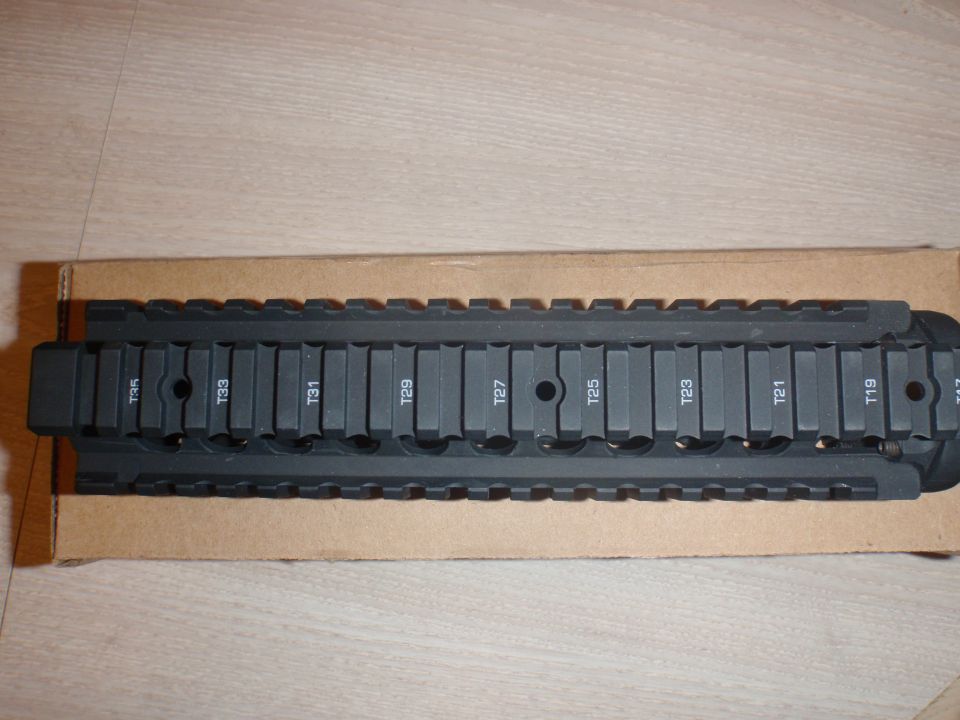 Black tactical rail with numbered slots, resting on cardboard