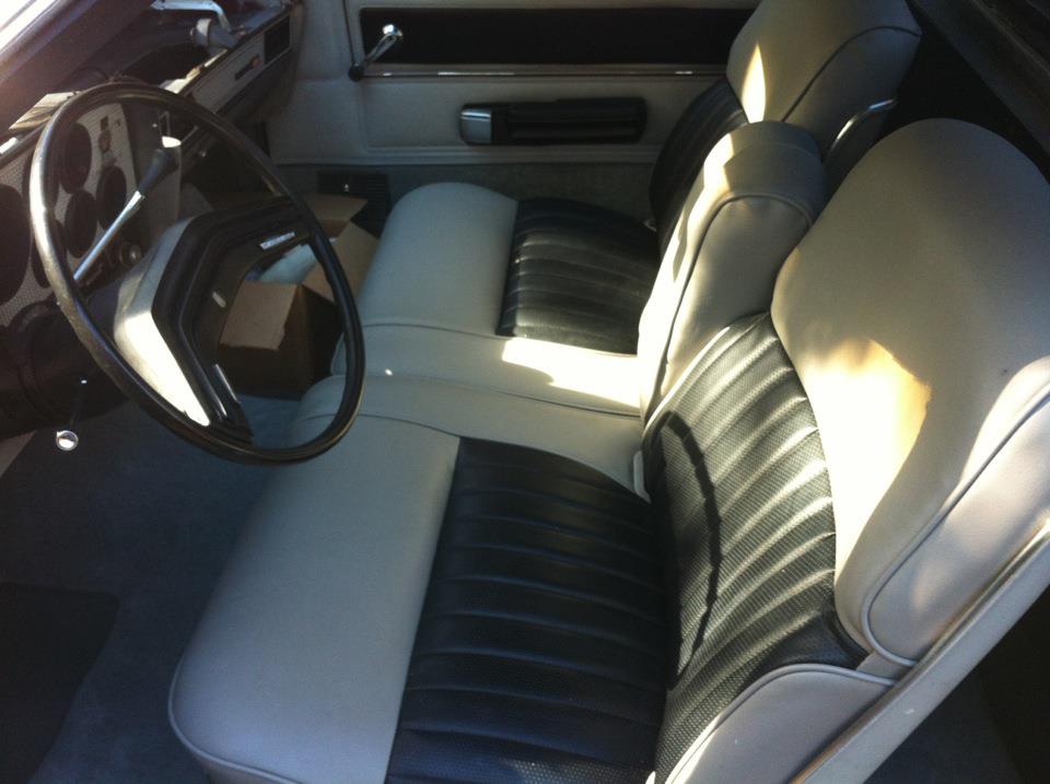 Interior shot of a car with two-tone seats, steering wheel, and dashboard visible. A box is on the floor