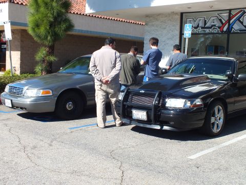 2003 Ford Crown Victoria - Men gather between a gray Crown Victoria and a black one with push bar outside Maxco body shop.