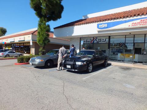 2003 Ford Crown Victoria - Two Crown Victoria sedans angled into spaces in front of the Maxco Paint and Body storefront.
