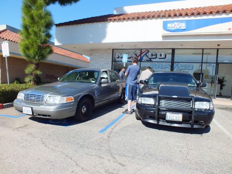 2003 Ford Crown Victoria - Gray Crown Victoria beside a black one with grille guard and EVIL VIC plate at the Maxco shop.