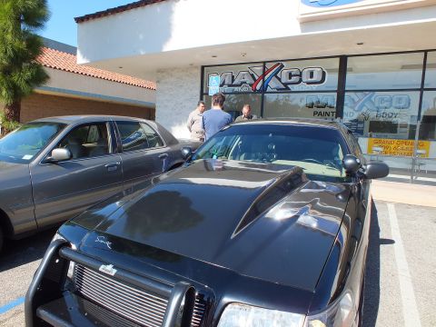 2003 Ford Crown Victoria - Front of a black Crown Victoria with grille guard outside Maxco; men talk by the grand-opening sign.