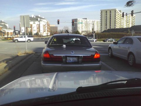 2003 Ford Crown Victoria - A Mercury Grand Marquis is seen from behind at a traffic light, with other vehicles and buildings in the background.