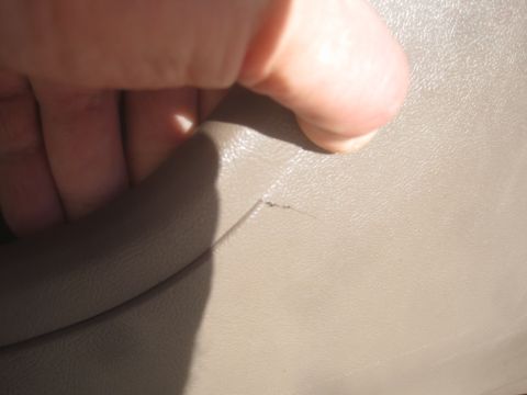 1993 Ford Bronco - A close-up of cracked tan interior trim, with a hand visible.