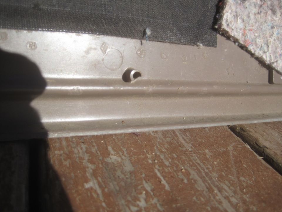 Close-up of a car's interior trim panel with a hole and some fabric lining