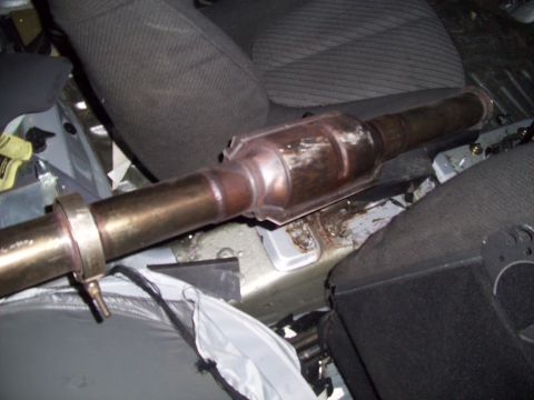 1995 Ford Probe - A catalytic converter is shown installed in the interior of a vehicle, likely under the seats. The catalytic converter is a metallic cylind…
